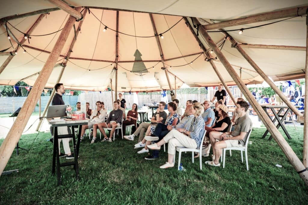 training-presentatie-onder-tent-venue13-evenement Presentatie tijdens een evenement bij Venue13 waarbij deelnemers luisteren naar een spreker onder een overdekte tent